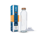 Botella flaska sport de vidrio con tapón de madera, su caja y pequeñas piedras blancas apiladas.