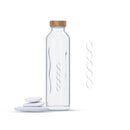 Botella de agua de vidrio con tapón de madera junto a piedras blancas apiladas y diseño energy flow.