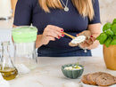 Mujer preparando una tostada saludable untando queso crema casero, con el fermentador de queso de Kéfir Kefirko de fondo.